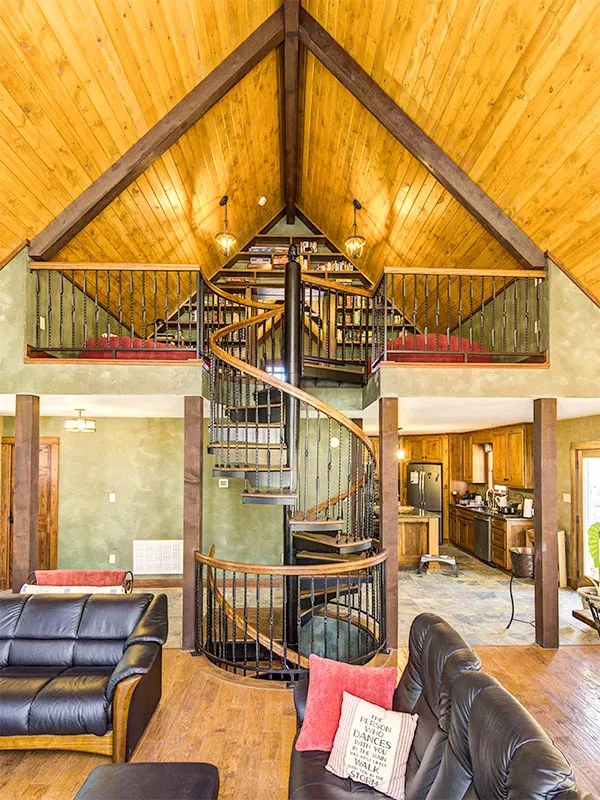 Forged iron spiral staircase with wood treads centered in a vaulted great room, serving as a dramatic focal point beneath warm wood ceilings.