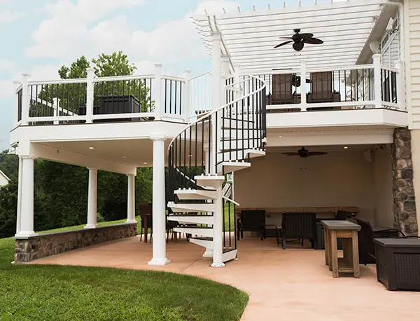 Powder-coated white aluminum spiral staircase connecting an elevated deck to a covered patio, creating a clean architectural focal point in an outdoor living space.