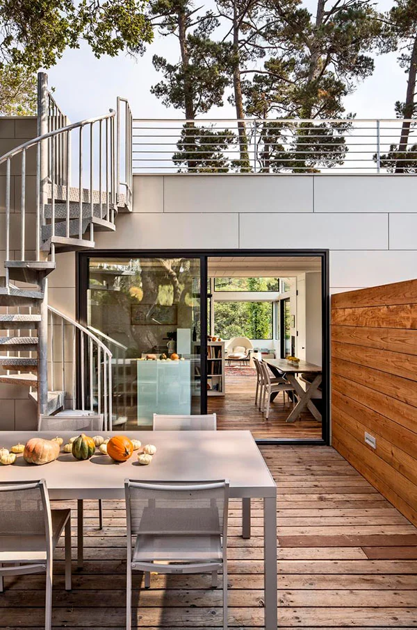Galvanized steel spiral staircase connecting rooftop deck and patio in a modern container home.