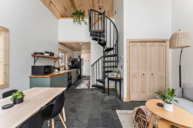 Black steel spiral staircase in a modern prefab cabin interior with natural wood finishes and an open loft.