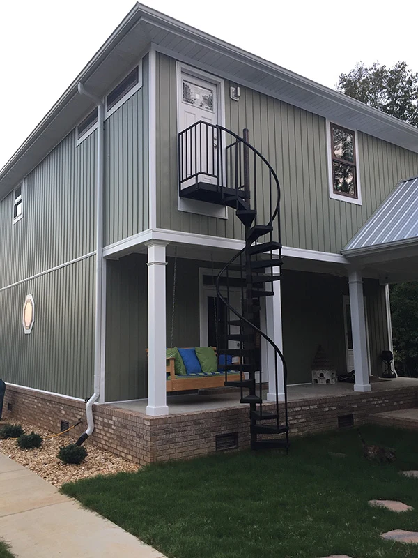 Black aluminum spiral staircase providing exterior access between levels of a modern modular home.