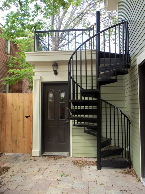 Black powder-coated aluminum spiral staircase providing exterior access to a small backyard ADU or tiny home.